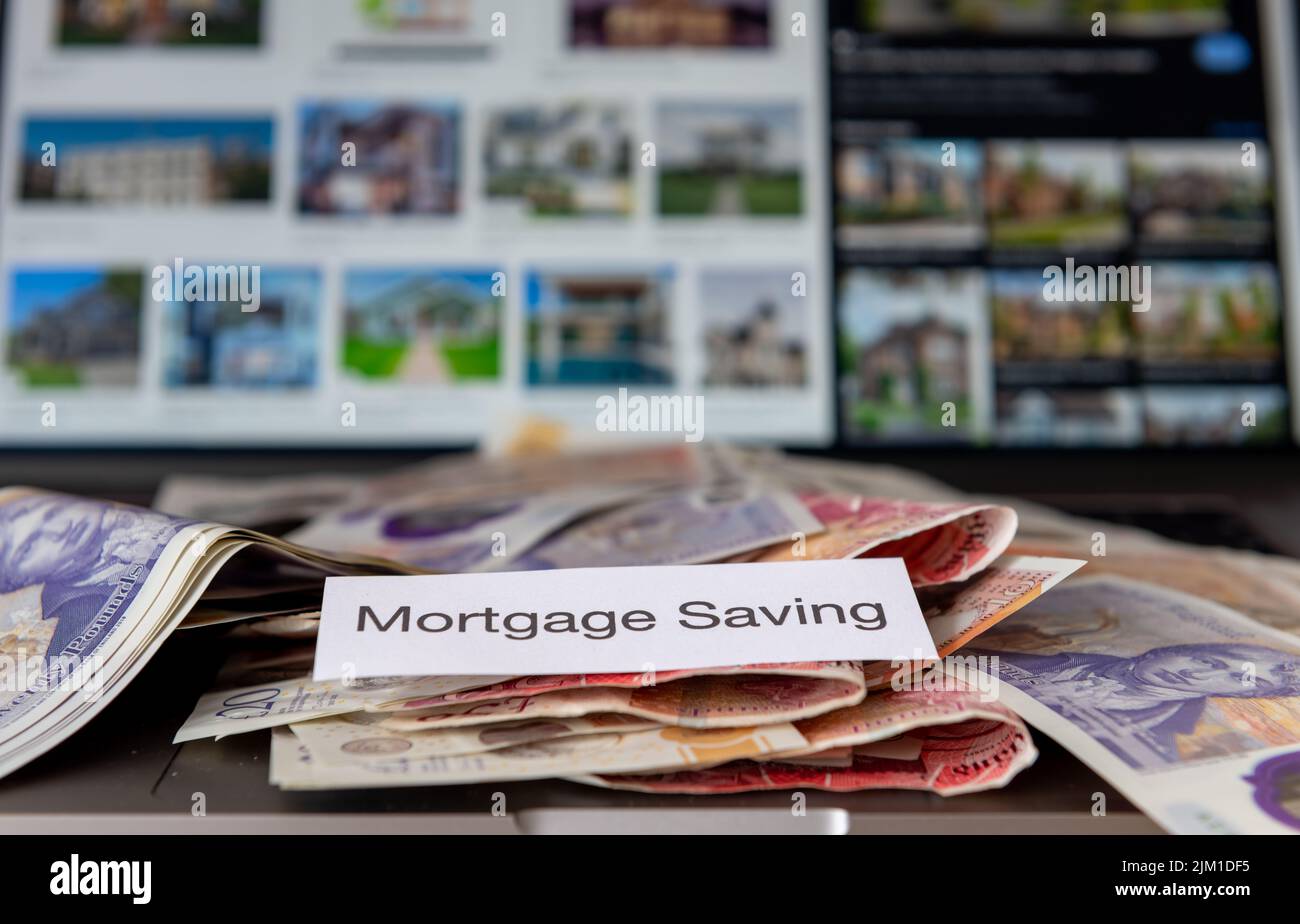 Un concepto de ahorro hipotecario con billetes de banco e imágenes borrosas de propiedades en un ordenador en el fondo. Foto de stock