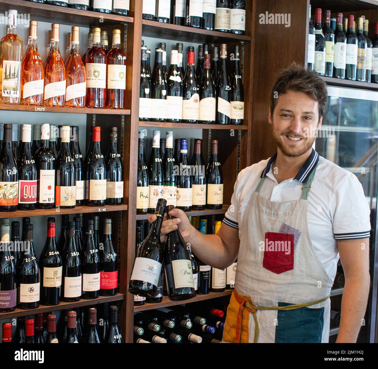 vendedor masculino con delantal parado en la tienda con vino Foto de stock