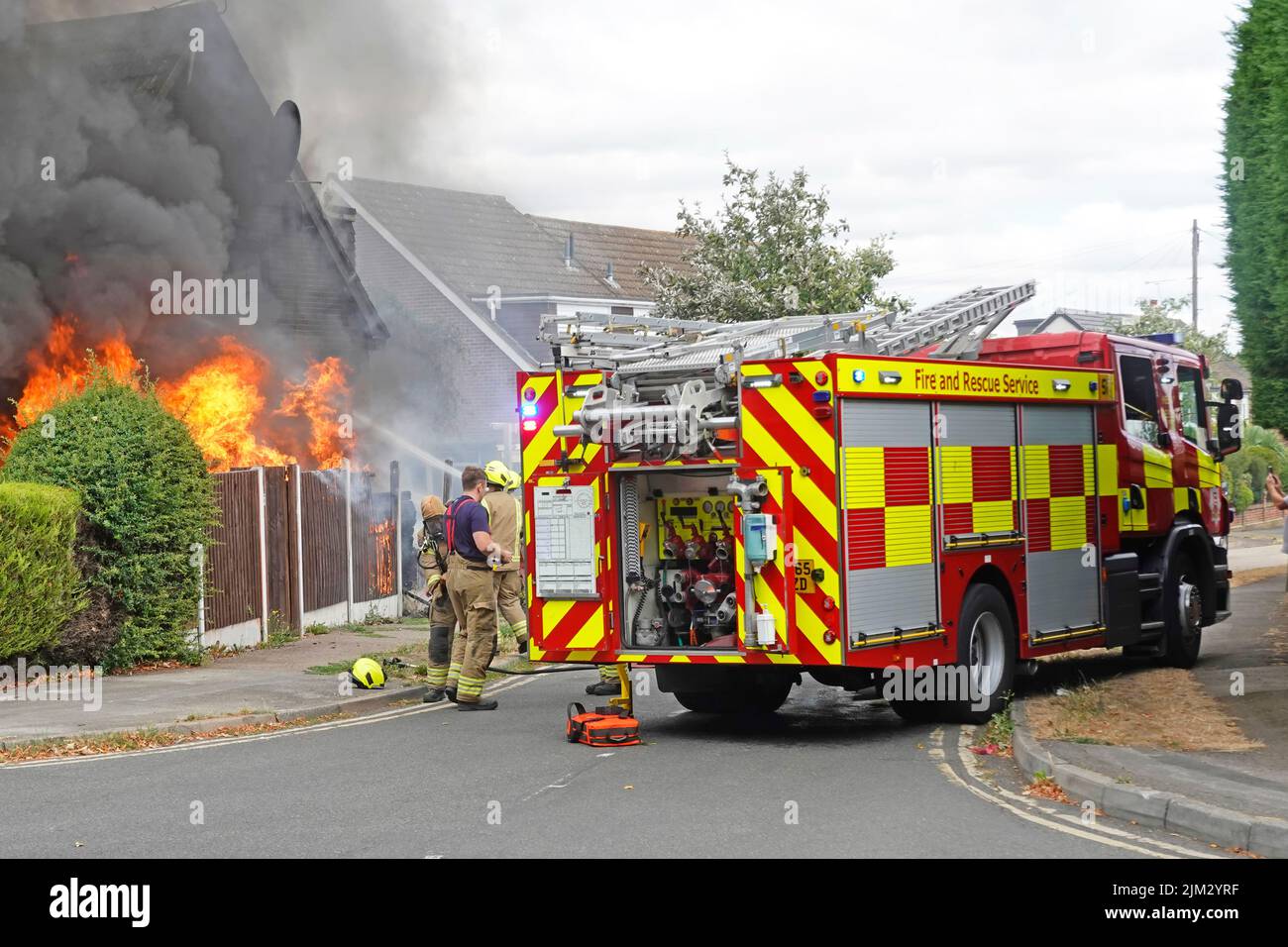 Llama y humo negro del fuego de la casa como bomberos llegar en la segunda brigada de bomberos motor tierno y tripulación llegar a trabajar en la calle residencial Essex Inglaterra Reino Unido Foto de stock