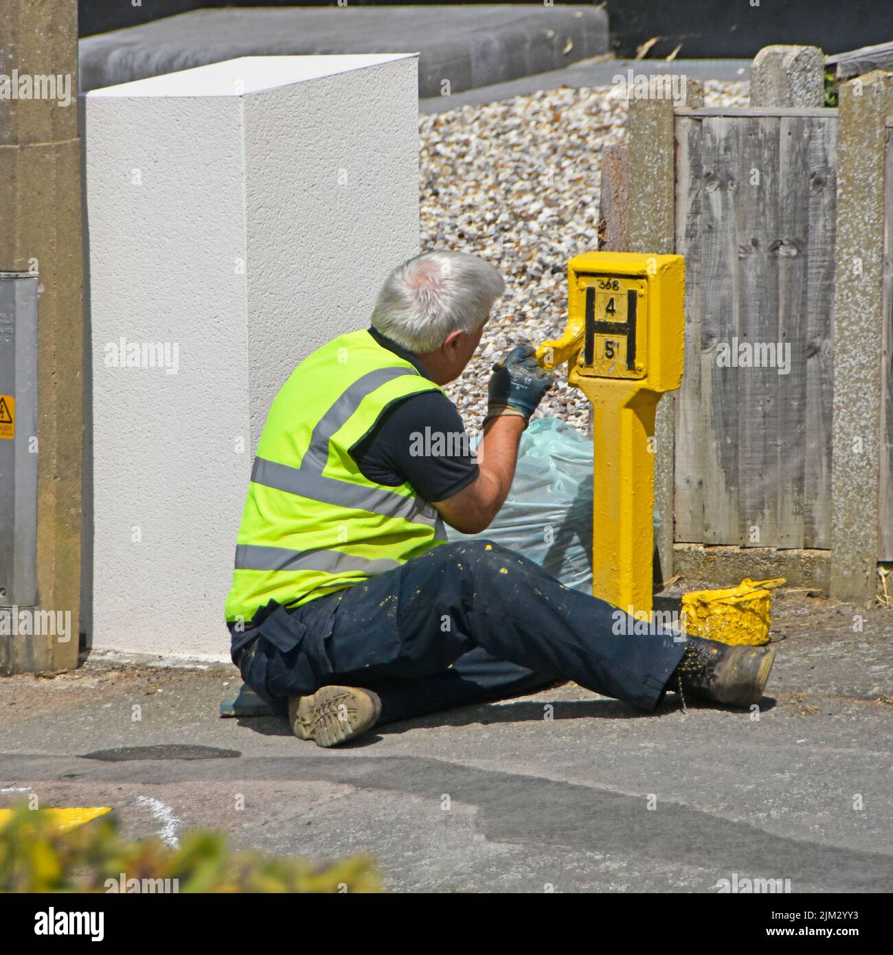 Obrero del Servicio de Bomberos y Rescate de Essex sentado en el pavimento con maceta de pintura amarilla letrero de hidrante callejero con chaqueta de alta visibilidad del Reino Unido Foto de stock