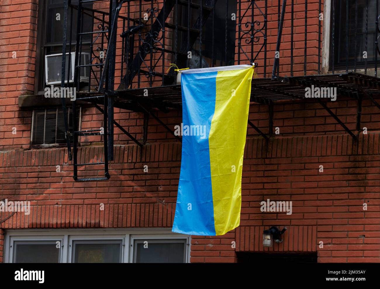 Una bandera ucraniana que cuelga de un escape de incendios frente a un edificio de ladrillo rojo en la ciudad de Nueva york, lo que demuestra solidaridad con Ucrania Foto de stock