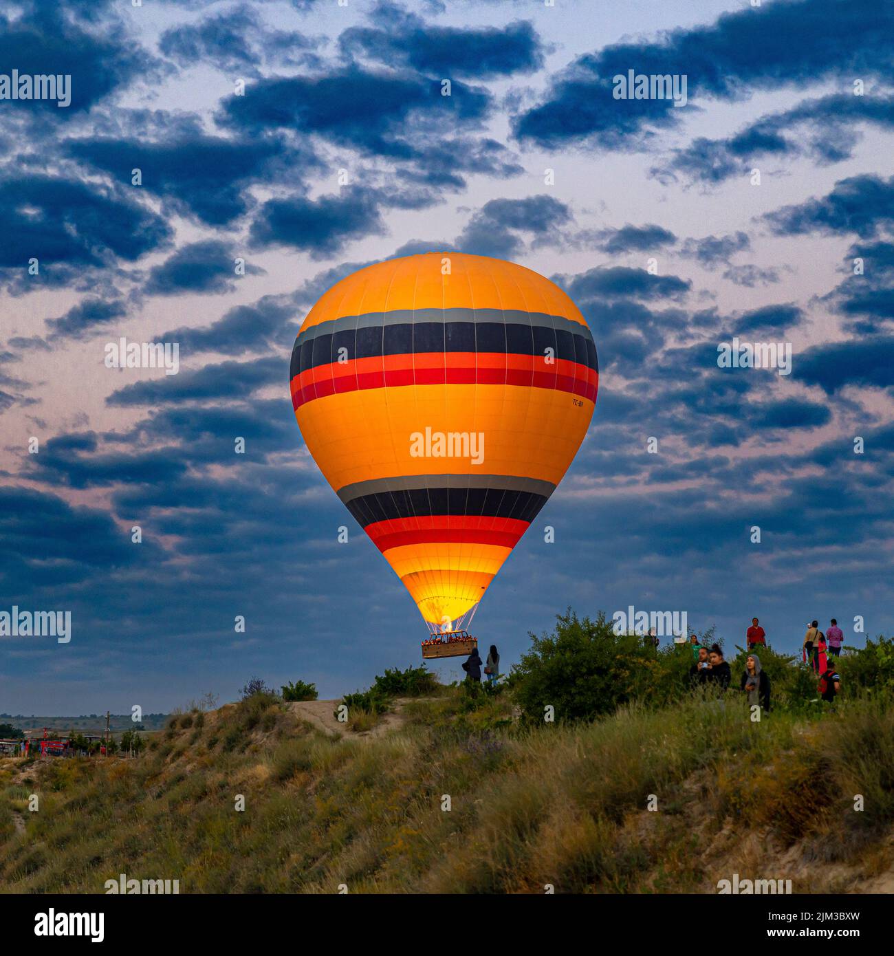 GOREME/TURQUÍA - 30 de junio de 2022: Un globo aerostático vuela sobre los turistas cerca de las colinas de goreme. Foto de stock