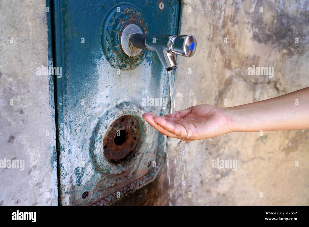 Cerca de la mano de la mujer bajo el agua corriente de una fuente en la pared. Sediento y crisis del agua. Foto de stock