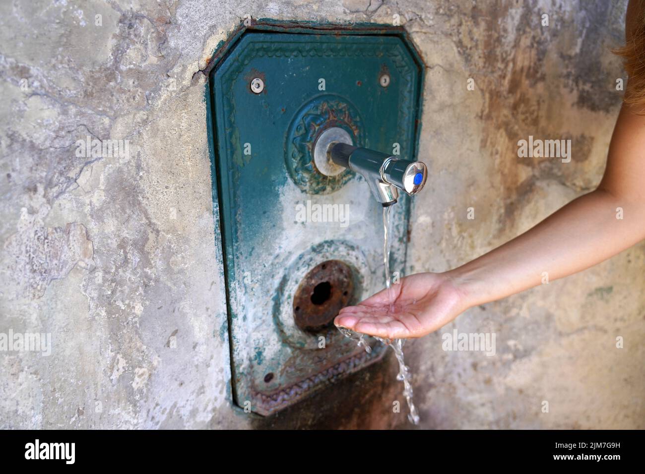 Cerca de la mano de la mujer bajo el agua corriente de una fuente en la pared. Sediento y crisis del agua. Foto de stock