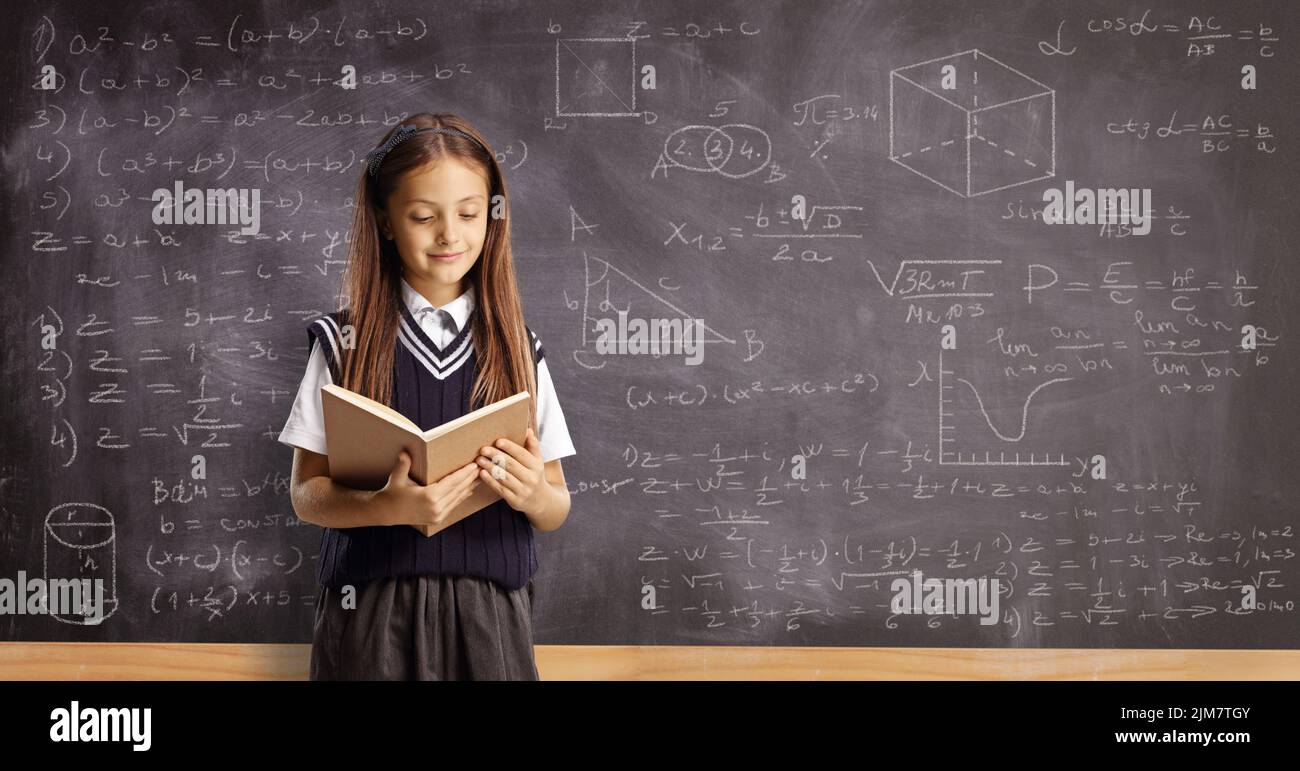 Alumno leyendo un libro y parado frente a una pizarra con geometría y fórmulas matemáticas Foto de stock