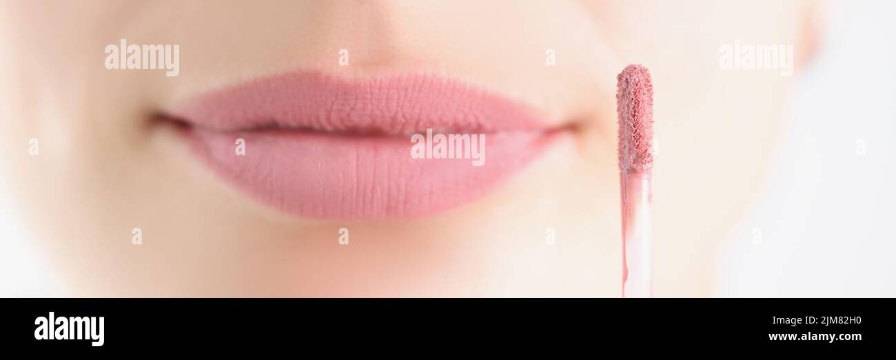 Pincel con brillo de labio mate rosa en la cara de fondo, primer plano Foto de stock