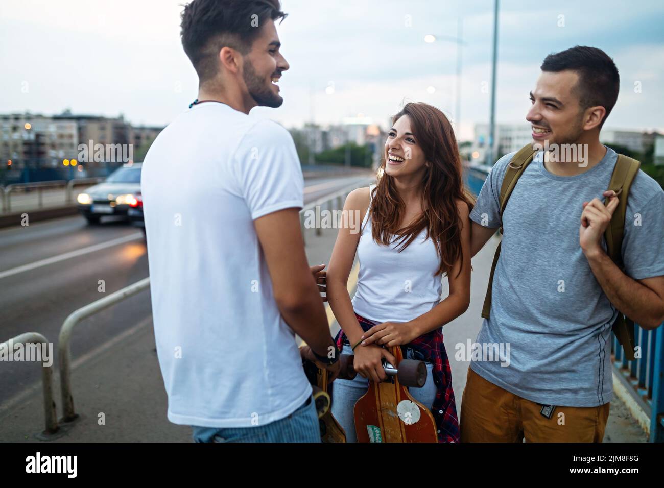 Retrato de adolescentes felices que se divierten mientras conducen un skateboard en la ciudad al aire libre. Foto de stock