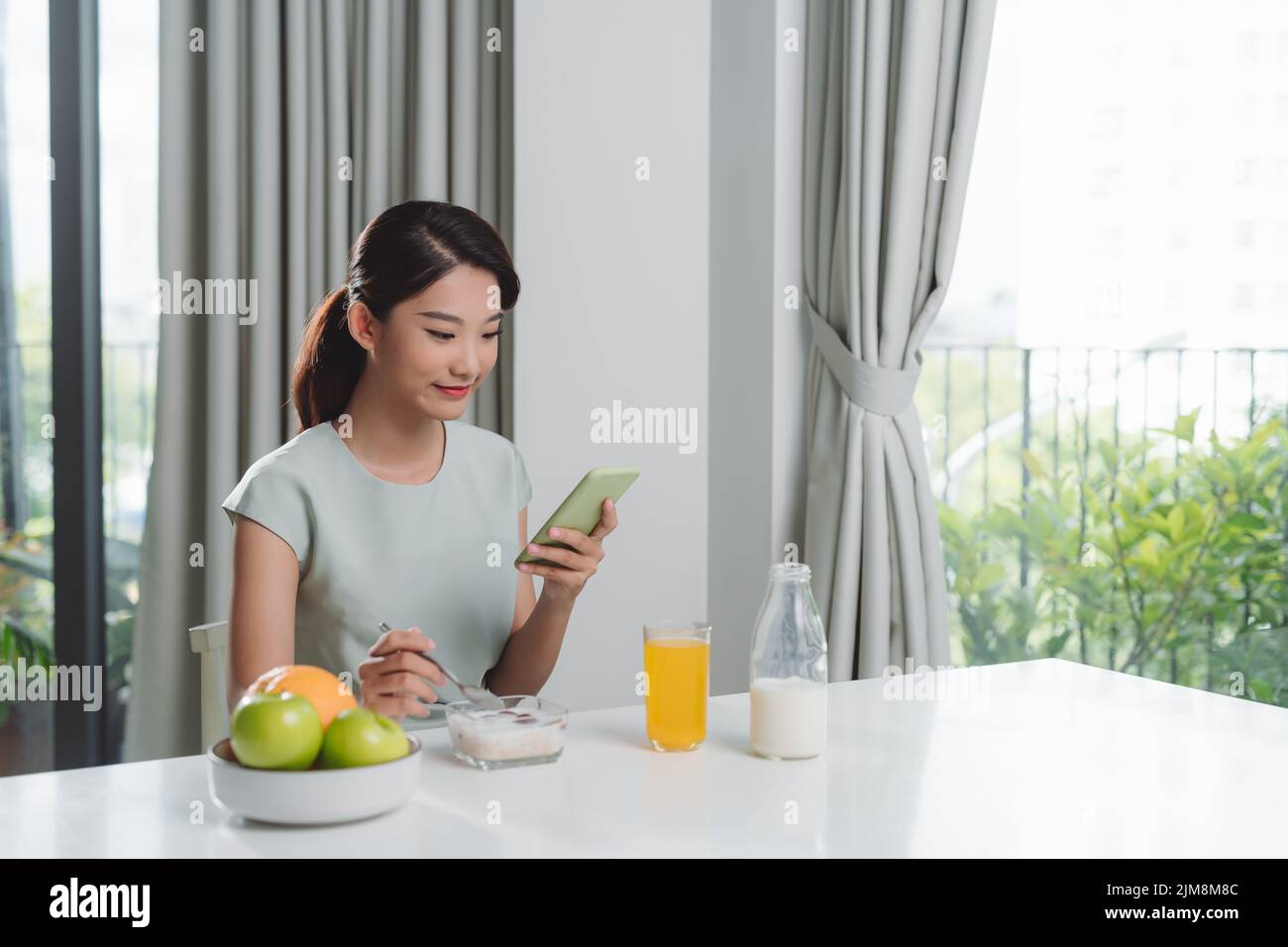 Mujer de comer un desayuno mientras utiliza el teléfono móvil Foto de stock