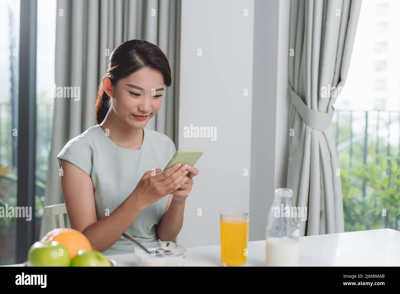 Hermosa mujer sonriente lindo está utilizando el teléfono inteligente en la cocina en casa. Foto de stock