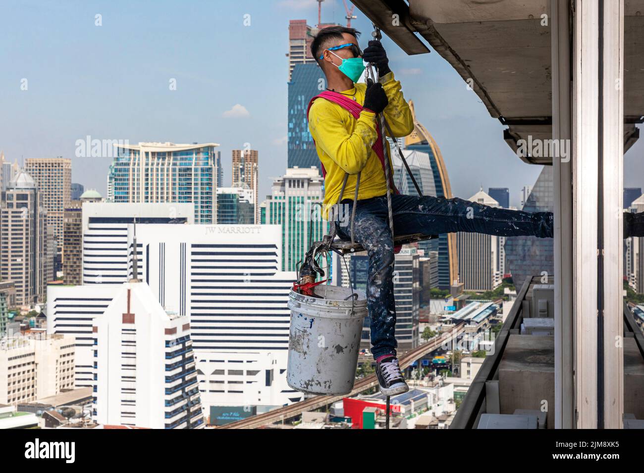 Obrero tailandés reparando ventanas en un edificio de gran altura con cuerda y polea, Bangkok, Tailandia Foto de stock