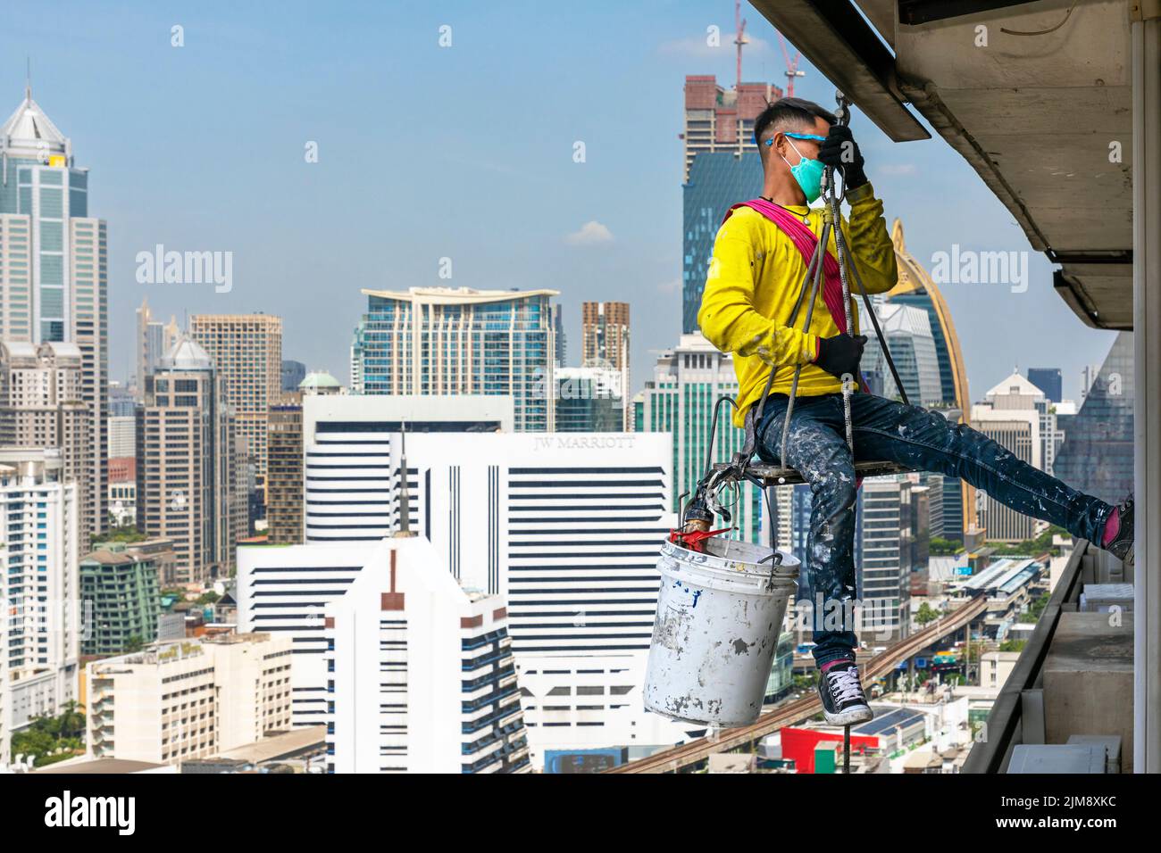 Obrero tailandés reparando ventanas en un edificio de gran altura con cuerda y polea, Bangkok, Tailandia Foto de stock