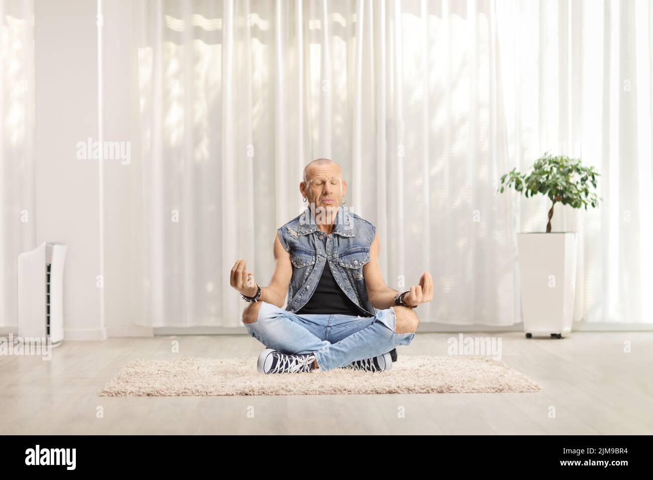 Hombre con vaqueros sentado en una alfombra haciendo yoga en la sala de estar de casa Foto de stock