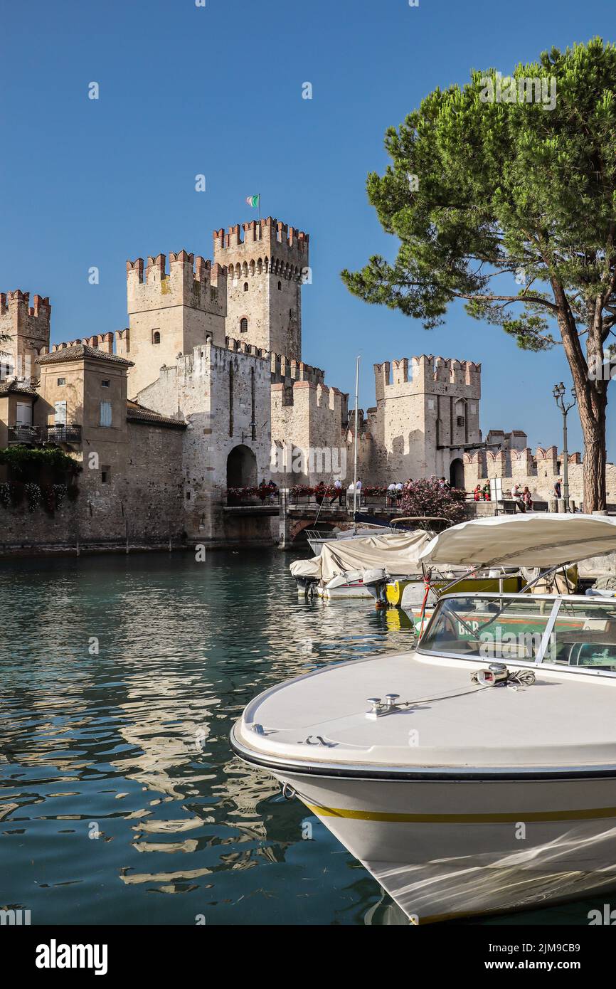 Sirmione, Italia - 25 de junio de 2022: Pequeño barco en el lago Garda con vistas al castillo Scaligero en Italia. Hermosa vista vertical de la ciudad idílica en verano. Foto de stock