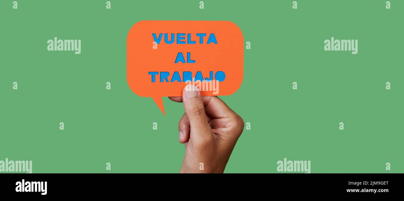 el hombre sostiene una burbuja naranja de discurso de papel con el texto de vuelta al trabajo escrito en español, sobre un fondo verde, en un formato panorámico para utilizar como web bann Foto de stock