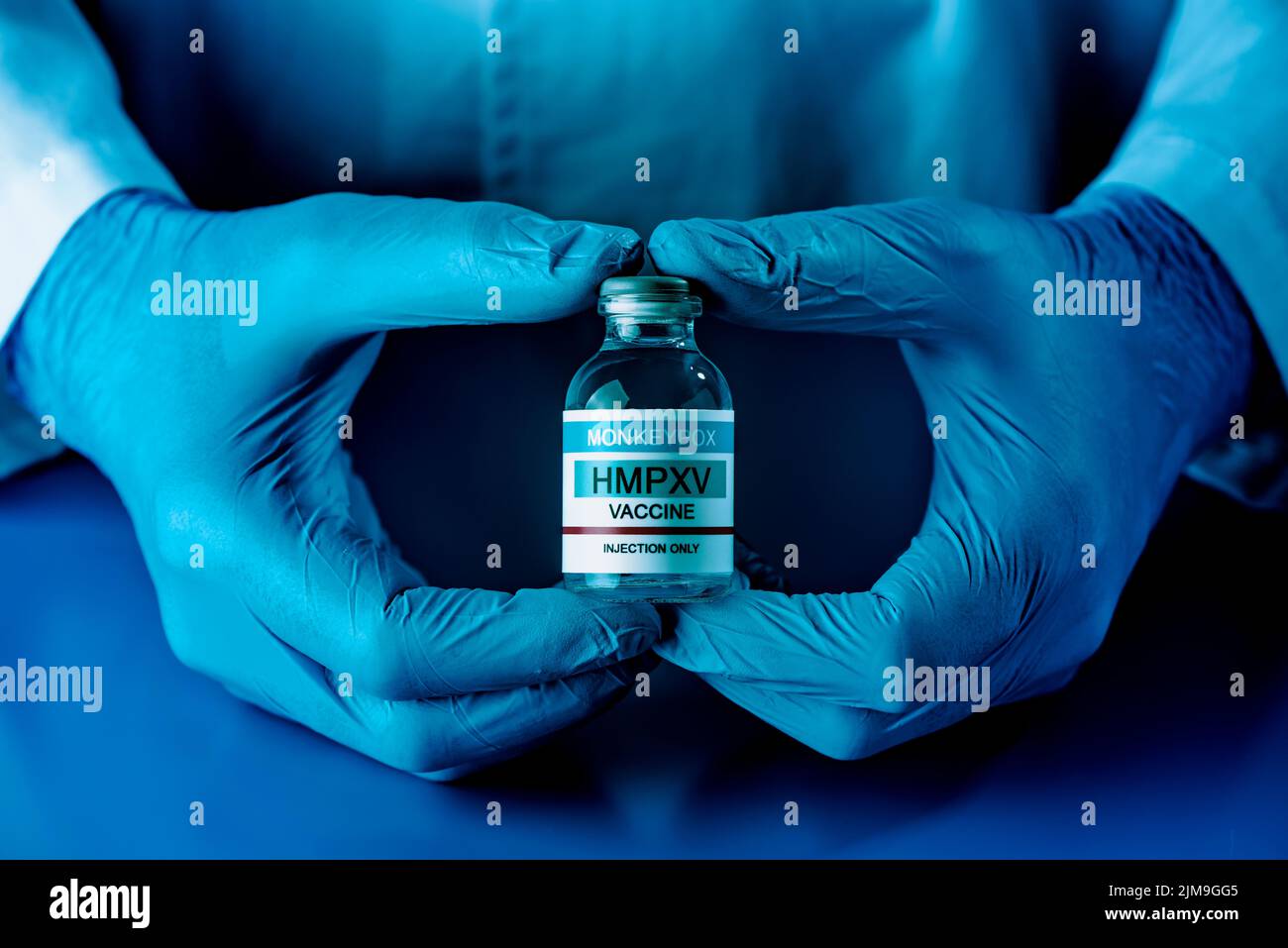 primer plano de un trabajador de salud o de laboratorio, con guantes quirúrgicos azules y un vial simulado de la vacuna contra la viruela del simio Foto de stock