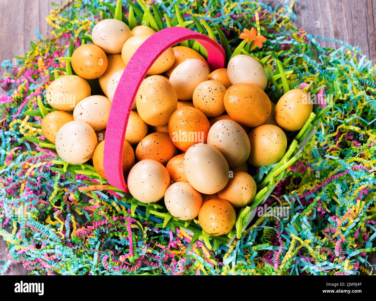 Huevos de Pascua en la cesta encima de colorido papel Mache con rústicas tablas de madera Foto de stock