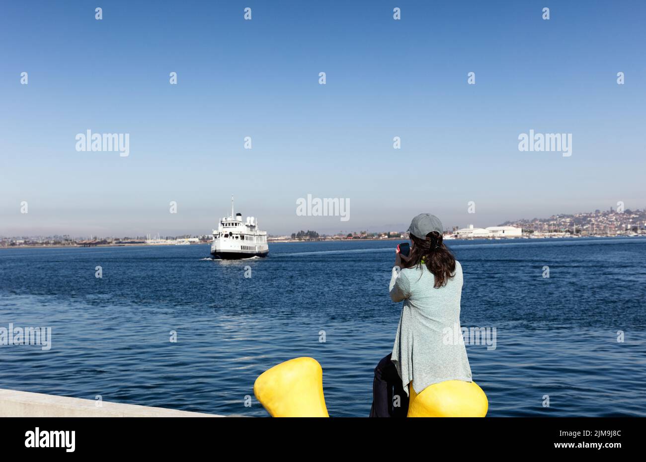 Mujer tomando fotos de la bahía de San Diego mientras se sienta en el muelle Foto de stock