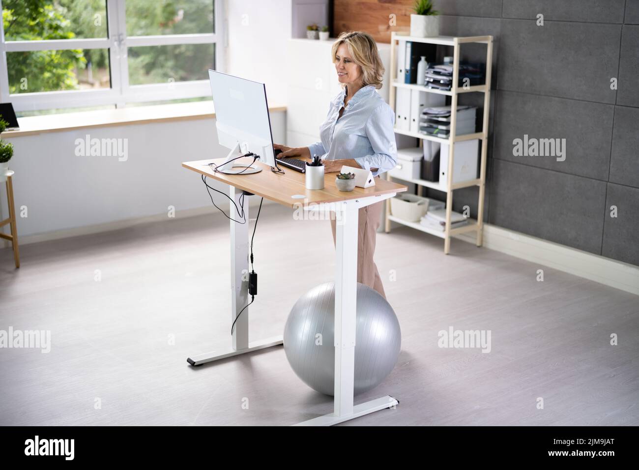 Mujer que usa el escritorio de pie de altura ajustable en la oficina para una buena postura Foto de stock