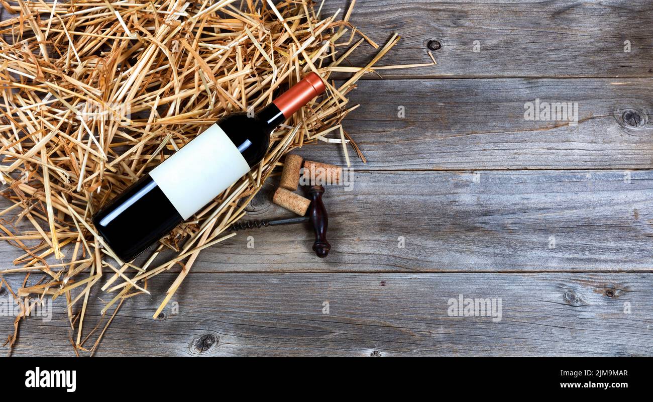 Botella de vino tinto con sacacorchos de vino vintage sobre paja y madera rústica Foto de stock