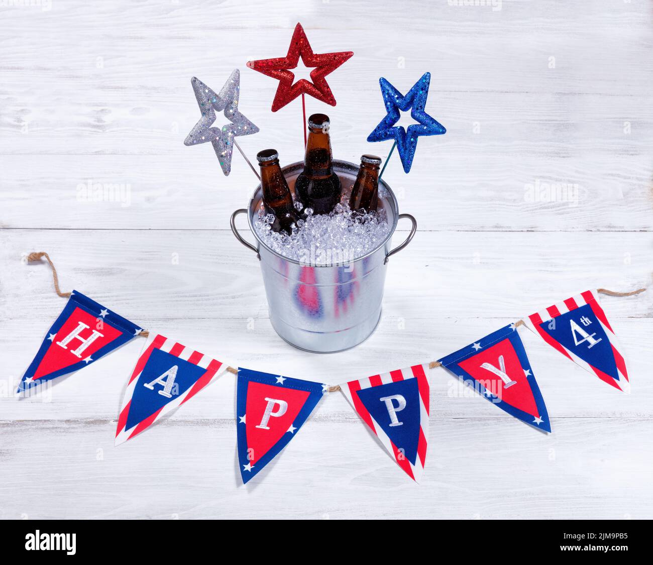 Estrellas de vacaciones y bandera con un cubo de metal de cerveza fría sobre madera blanca rústica Foto de stock