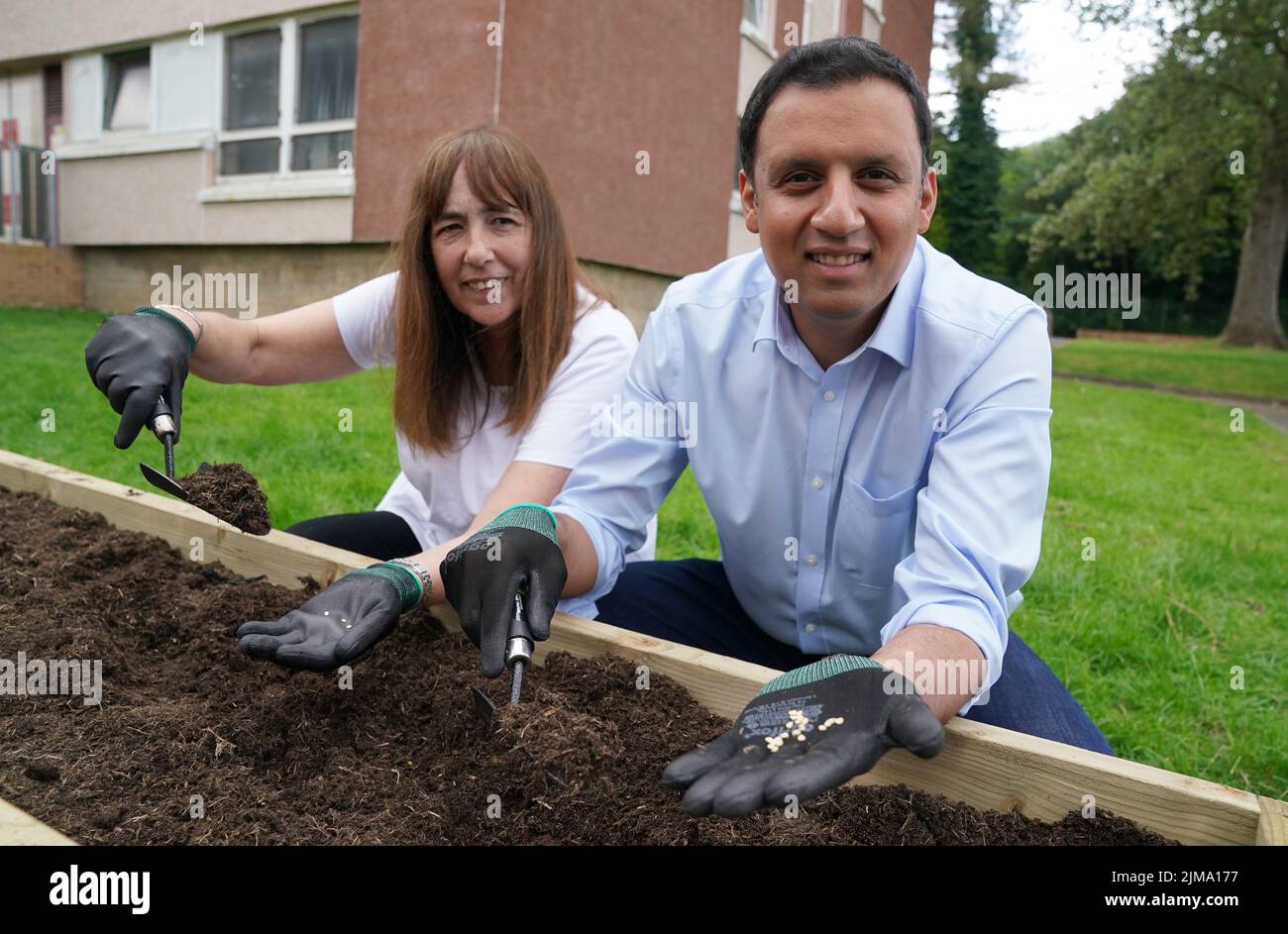 El líder laborista escocés Anas Sarwar ayuda a Sharon Bowers a plantar semillas en un jardín comunitario durante su visita al Acre Community Hall, Glasgow, donde conoció a voluntarios en el banco de alimentos y luego plantó semillas en un parche vegetal. Fecha de la foto: Viernes 5 de agosto de 2022. Foto de stock