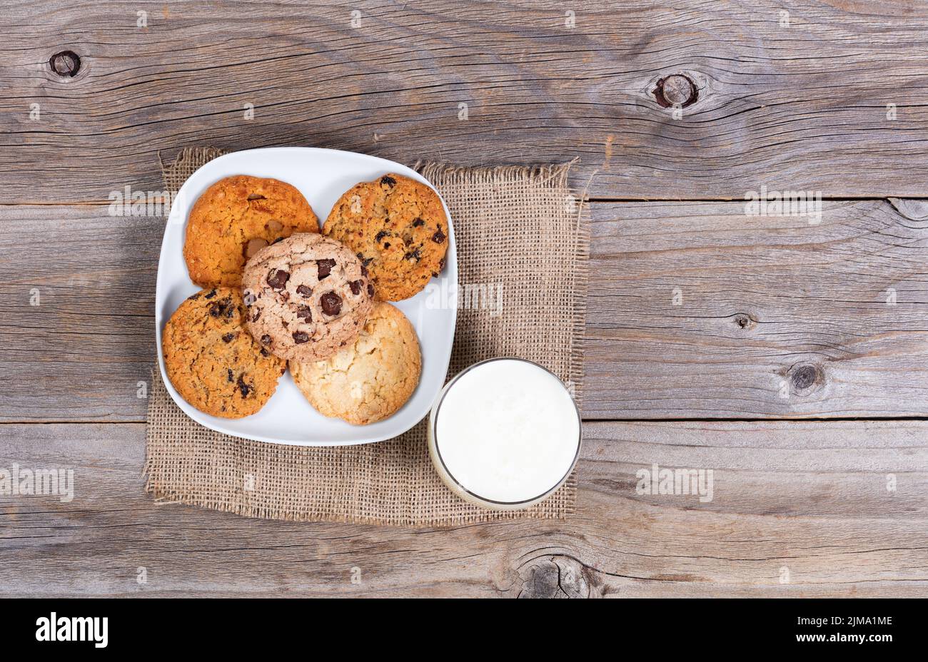 Variedad de galletas horneadas en servilleta y vaso de leche sobre rústicas tablas de madera Foto de stock
