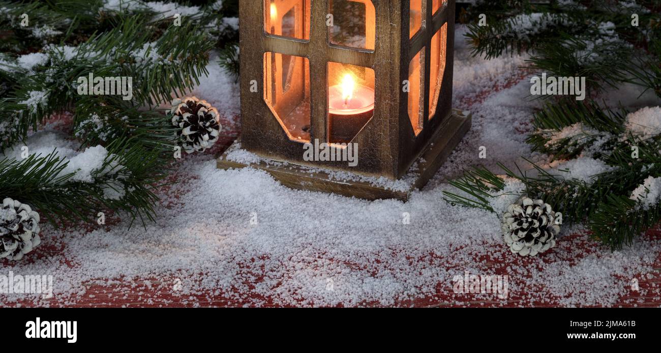 Linterna vintage con vela encendida sobre tablas de madera roja rústica nevada con decoraciones navideñas Foto de stock
