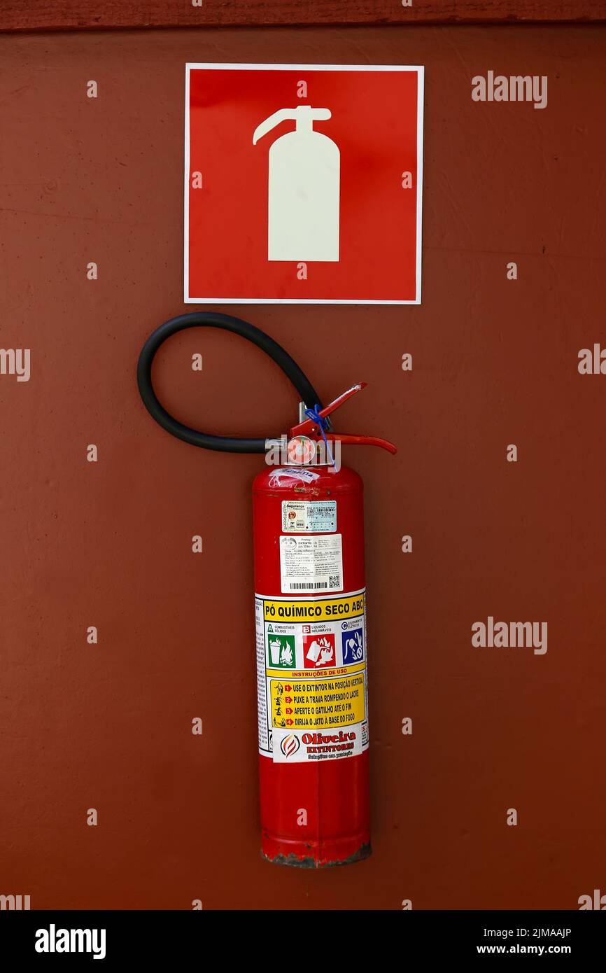 Minas Gerais, Brasil - 10 de julio de 2022: Extintor debajo de la señal en la pared roja Foto de stock