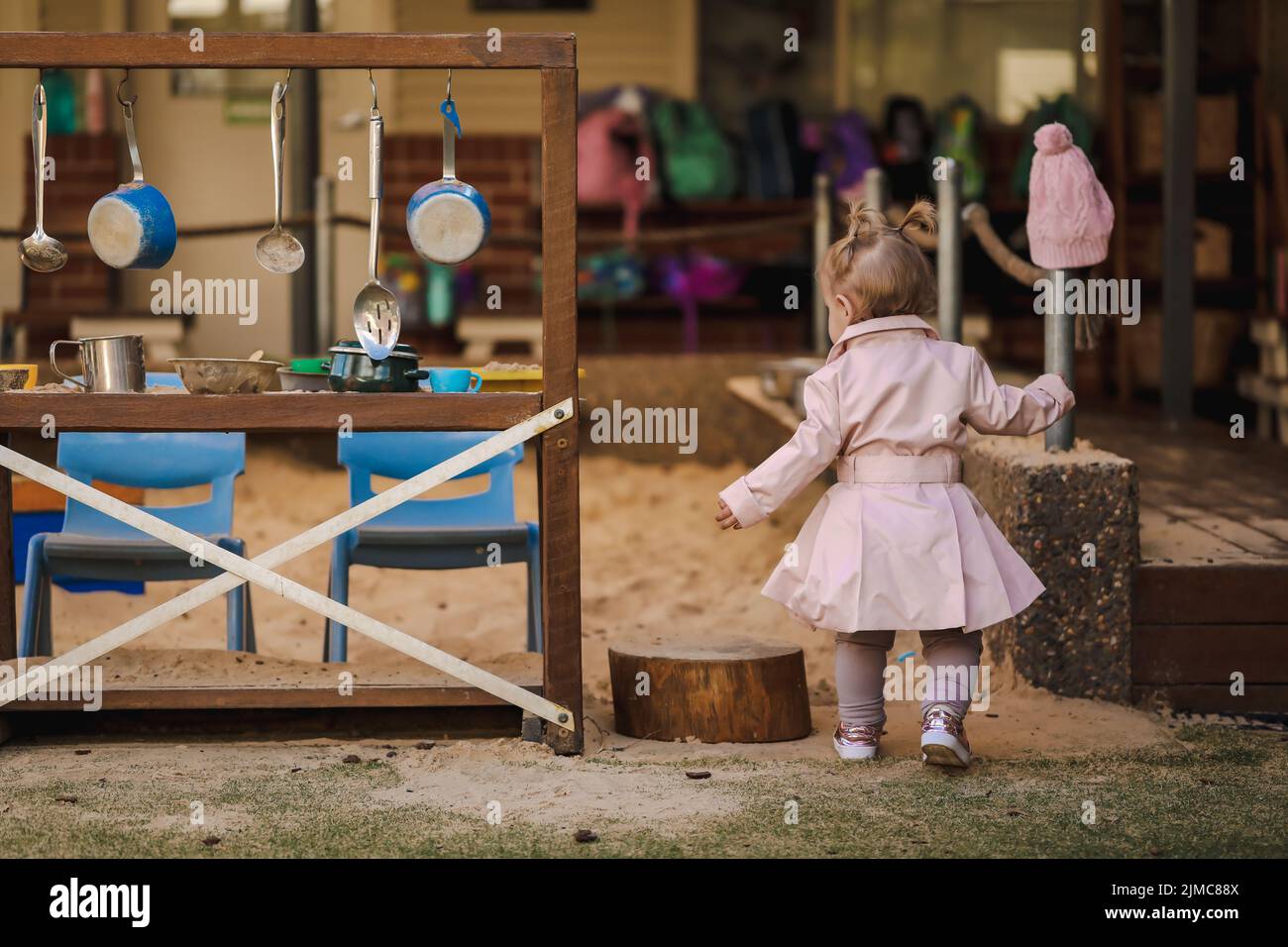 Niña pequeña con pigtails en el centro de cuidado diurno usando lindo abrigo rosa, sin cara Foto de stock