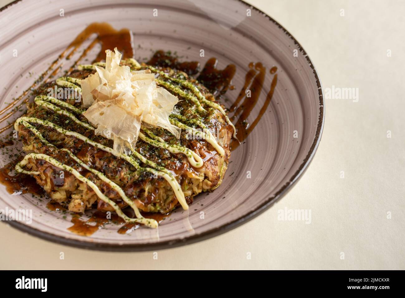 Desde arriba de un sabroso plato tradicional japonés okonomiyaki con salsa cubierta con copos de bonito servido en un cuenco de cerámica sobre fondo claro Foto de stock