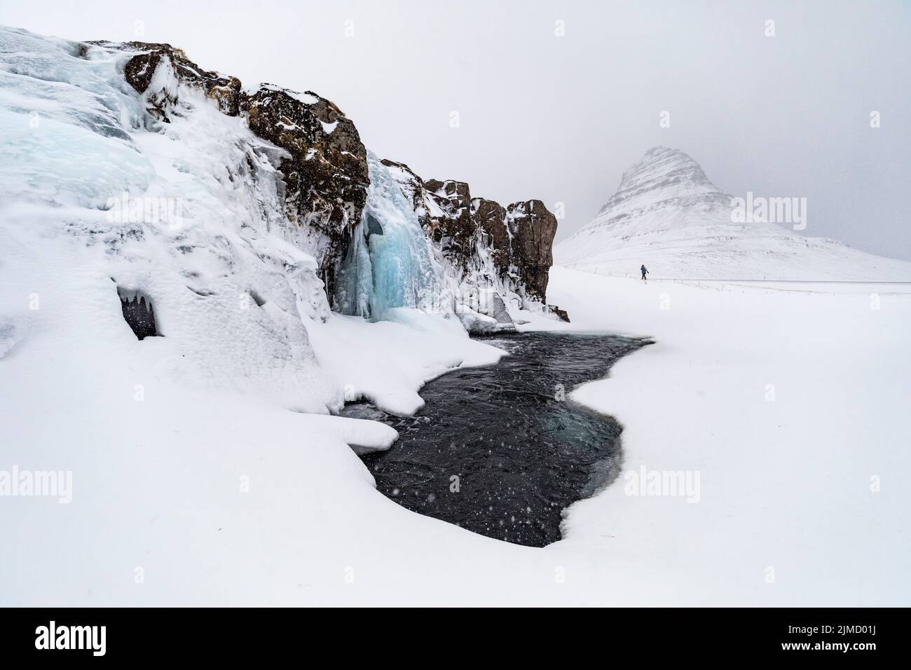 Viajeros lejanos caminando en la costa montañosa del lago congelado ubicado en el terreno nevado de las tierras altas en Islandia Foto de stock