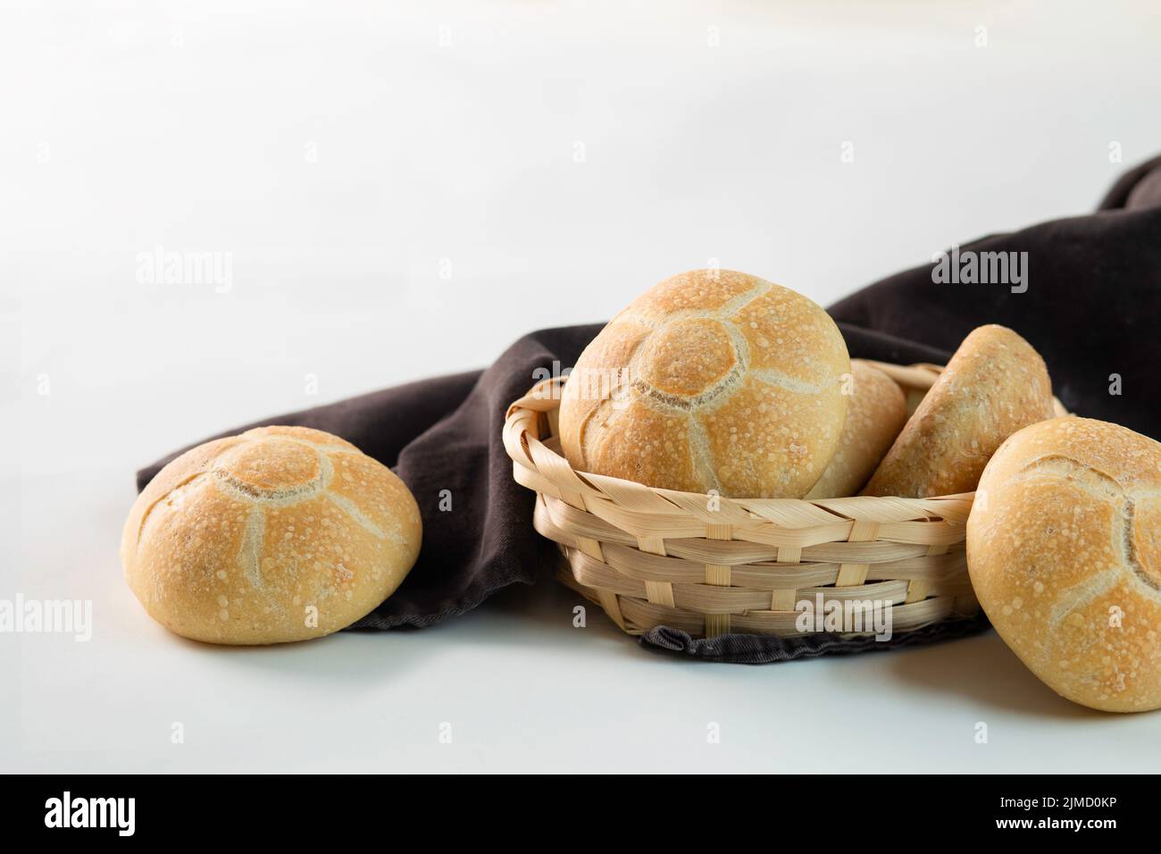 Deliciosos bollos recién horneados colocados en un tazón de mimbre cerca de tela marrón sobre fondo blanco Foto de stock