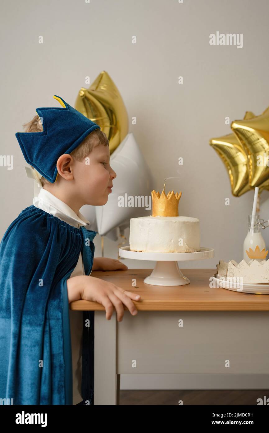 Vista lateral de un chico rubio soplando velas en una fiesta de cumpleaños Foto de stock