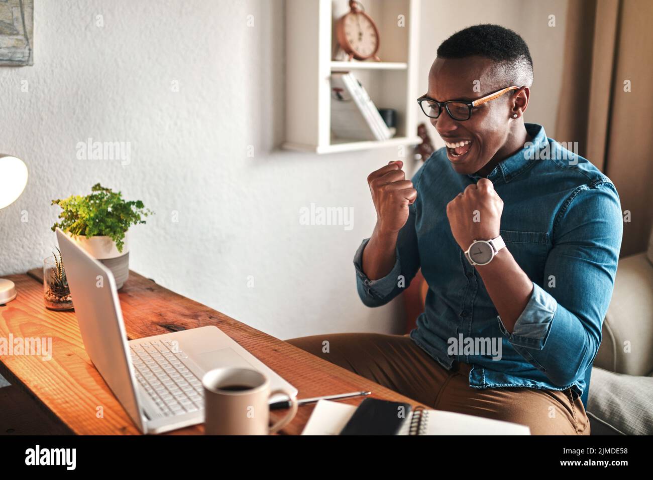 Hombre emocionado en una computadora en casa sintiéndose feliz, confidente y orgulloso sobre ganar un juego en línea de la tela del casino. Hombre sonriente disfrutando de una victoria digital en interiores Foto de stock