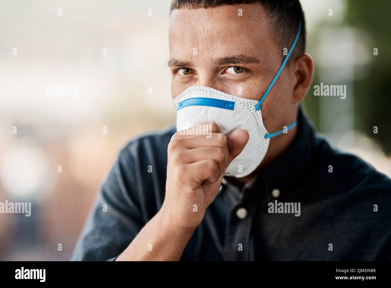 Oh no... un joven tosiendo y usando una máscara contra el fondo de la ciudad. Foto de stock