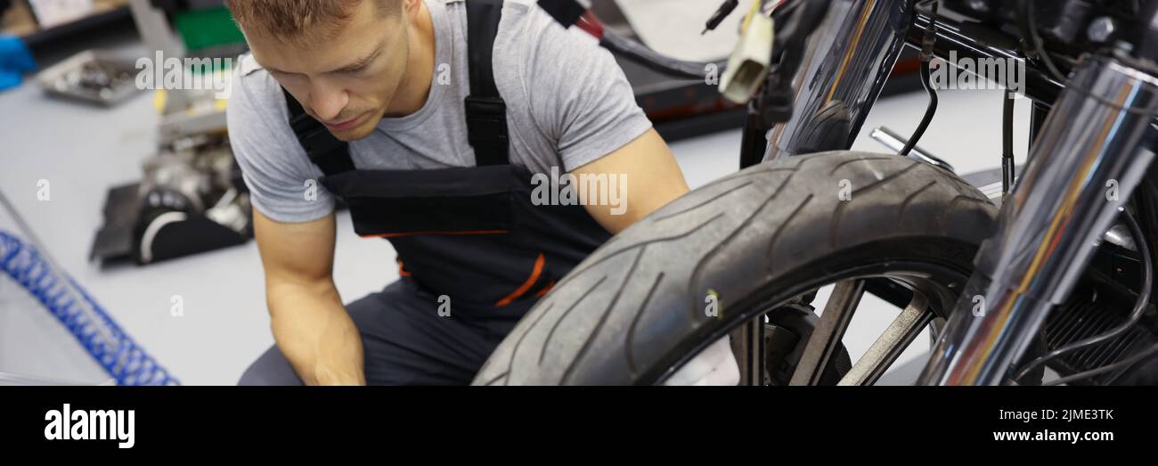 En el garaje, un reparador en overalls se encuentra cerca de la motocicleta de rueda Foto de stock