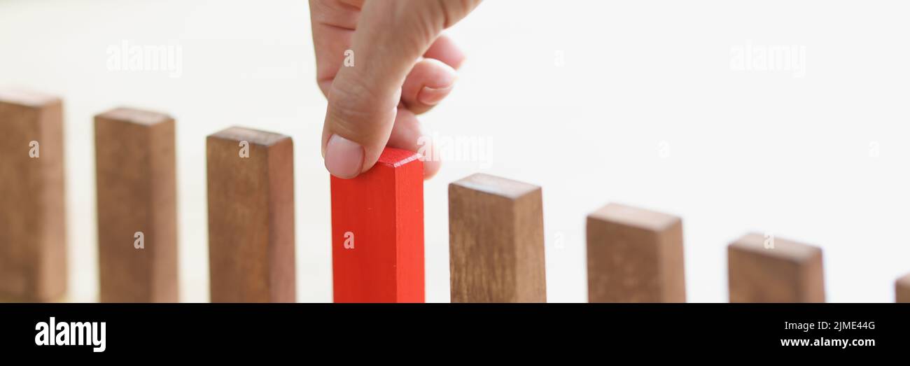 La mano pone sobre la mesa un bloque de madera rojo en fila con los marrones Foto de stock