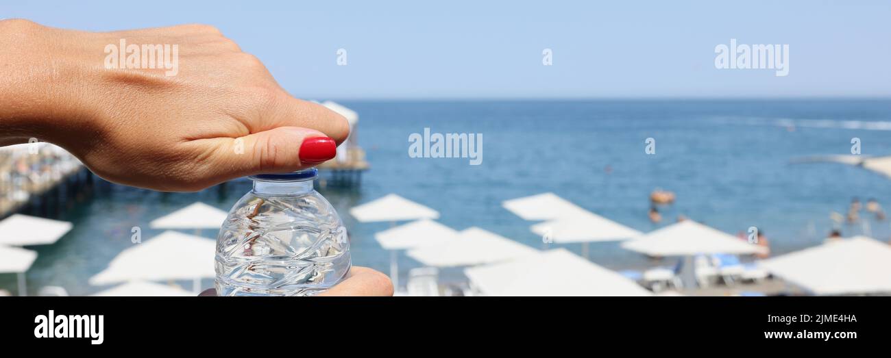 Las manos femeninas abren una botella de agua en una playa, borrosa Foto de stock