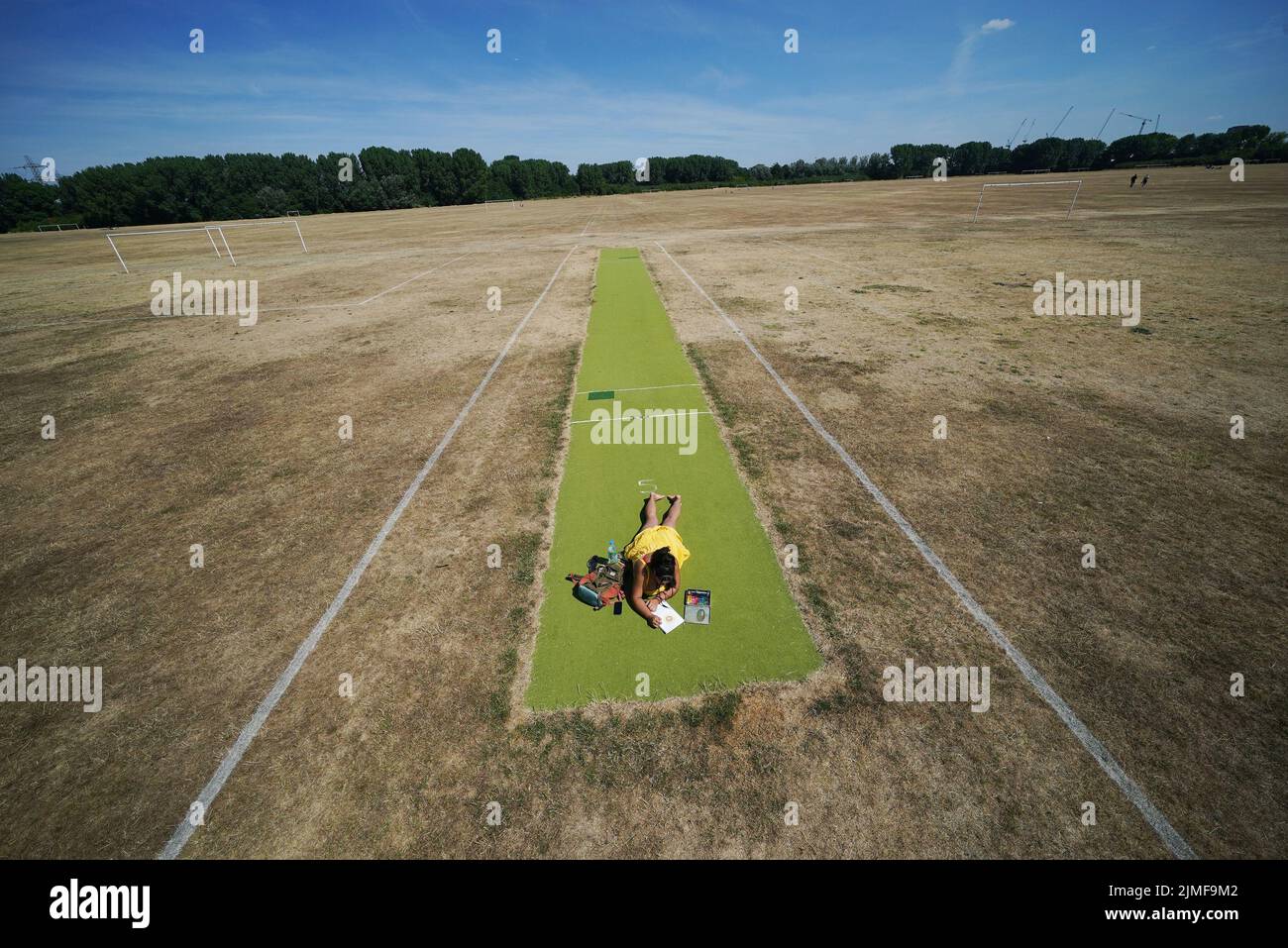 Una mujer se relaja en un campo de cricket verde rodeado de campos de fútbol, en Hackney Marshes, al este de Londres. Fecha de la foto: Sábado 6 de agosto de 2022. Foto de stock