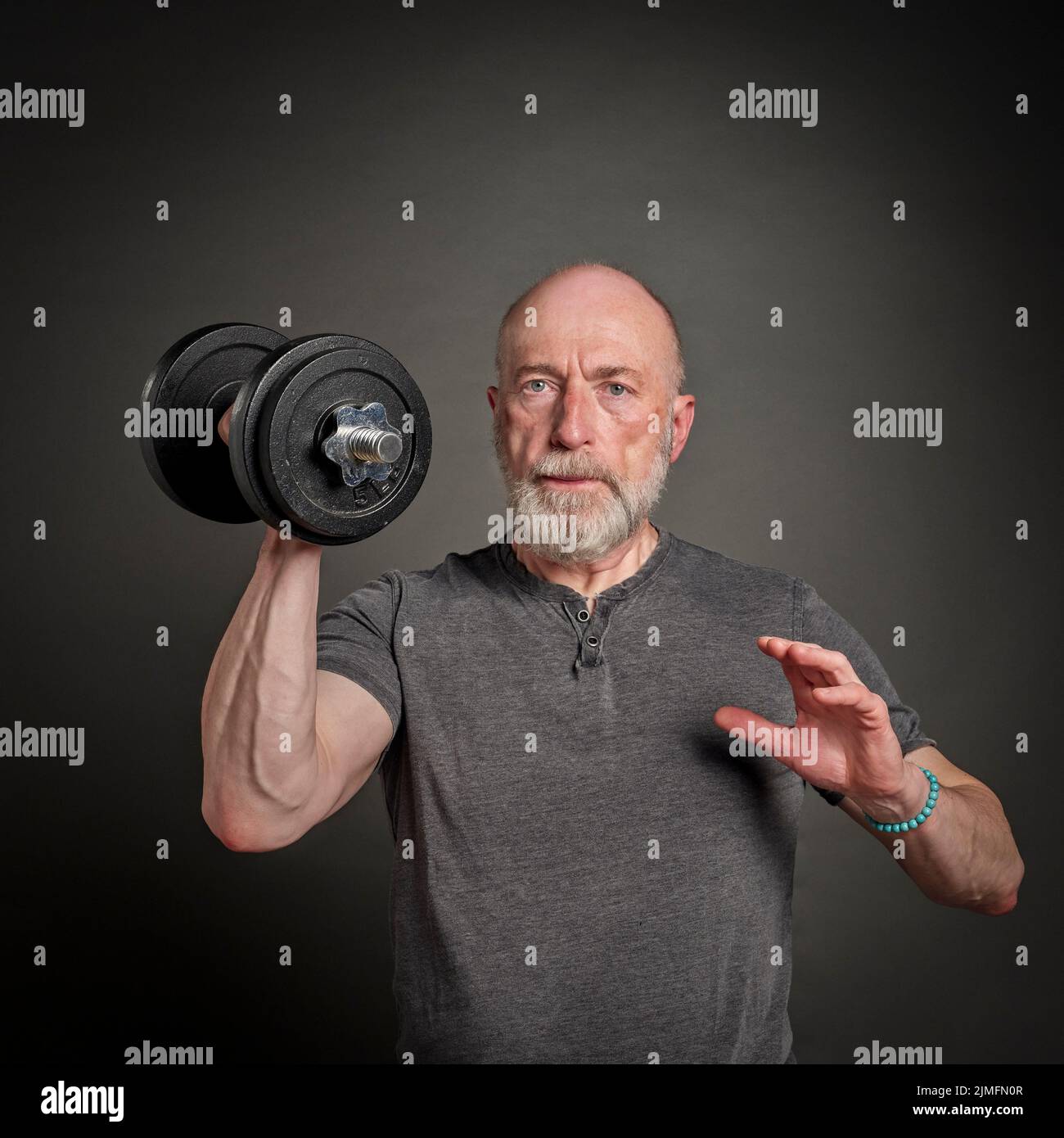 retrato casual de viejo hombre barbudo (a finales de 60s) haciendo ejercicio con dumbbell pesado, anciano activo y concepto de la aptitud Foto de stock
