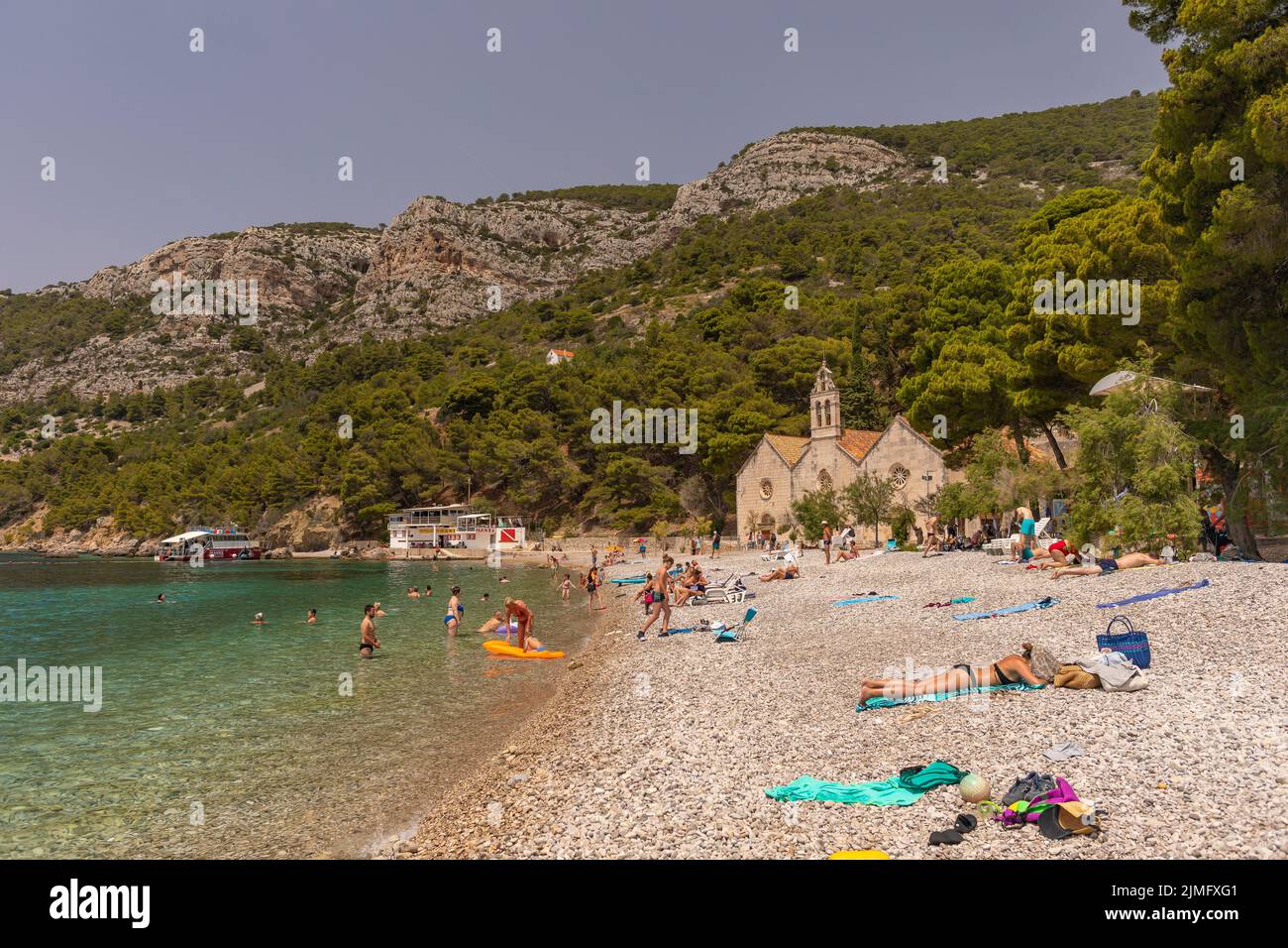 KOMIZA, VIS, CROACIA, EUROPA - La gente disfruta de la playa en la ciudad costera de Komiza, en la isla de Vis, en el mar Adriático. Foto de stock