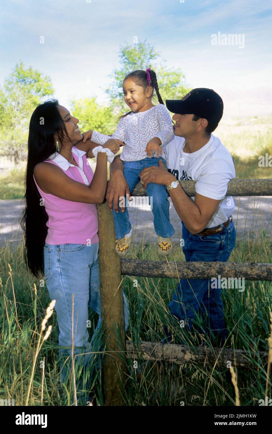 Familia nativa americana de una hija de 4 años con sus padres se sientan en un poste de granja y cerca de un carril. Foto de stock