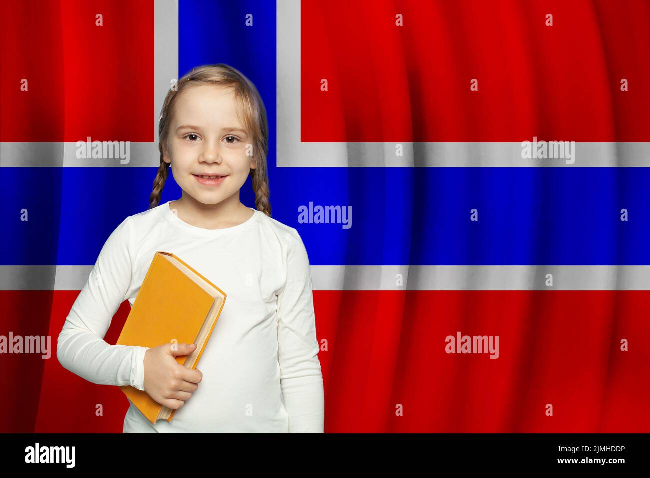 Niña divertida con libro contra la bandera de Noruega de fondo. Educación, escuela y concepto de lengua noruega. Foto de stock