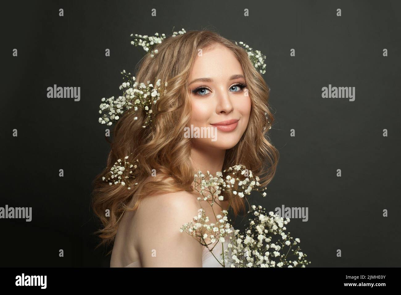Mujer rubia con el pelo largo y brillante ondulado sostiene flores Foto de stock