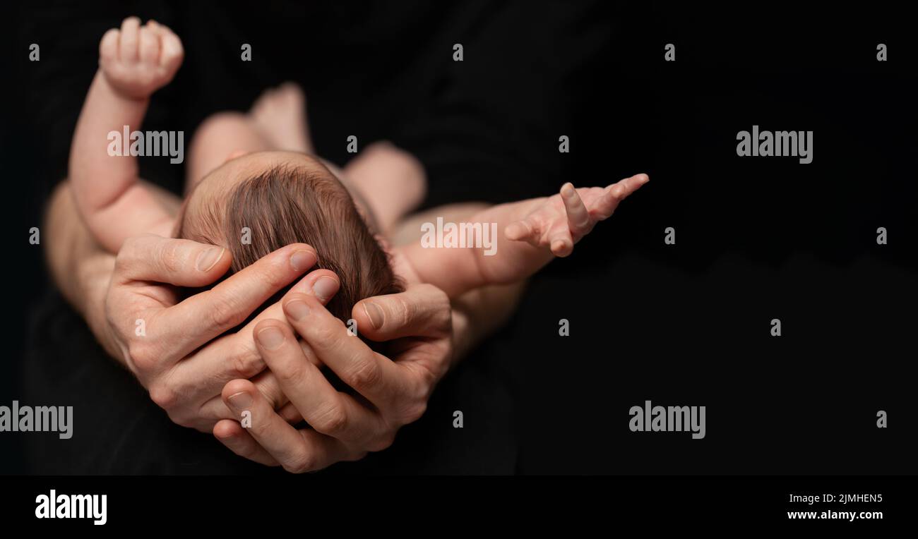 El padre sostiene al hijo recién nacido desnudo en sus manos sobre fondo negro Foto de stock