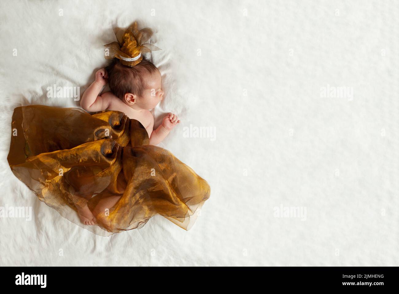 Adorable bebé princesa recién nacido en un pequeño vestido dorado sobre manta blanca Foto de stock
