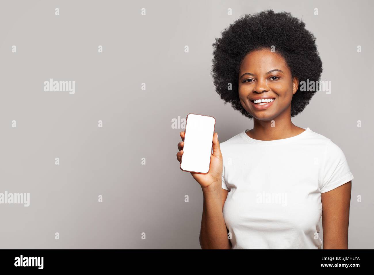 Retrato de mujer negra feliz en blanco camiseta smartphone con pantalla vacía en blanco sobre fondo blanco de la pared del estudio Foto de stock