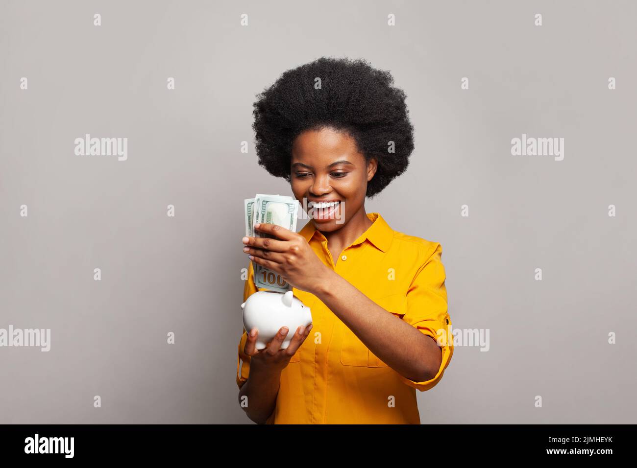 Mujer alegre con dinero del dólar americano y banco de dinero blanco sobre fondo gris Foto de stock