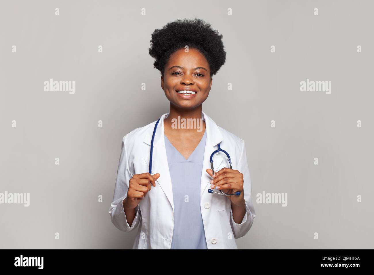 Amiga doctora usando abrigo blanco con estetoscopio mirando la cámara y sonriendo alegremente Foto de stock