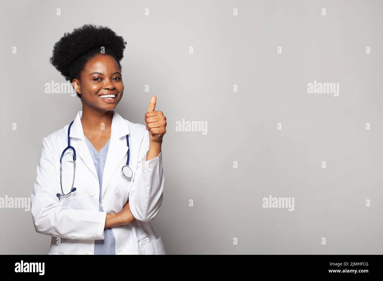 Joven mujer feliz confidente doctor mostrando pulgar para arriba sobre fondo blanco Foto de stock